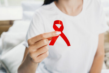 A woman holding a red ribbon symbolizing awareness on a soft, cozy bed during daylight
