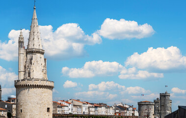 Obraz premium city of La Rochelle with a tall tower and a cloudy sky. The sky is blue and the clouds are white