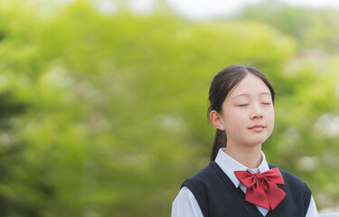 鮮やかなグリーンの木の前で目を閉じる少女