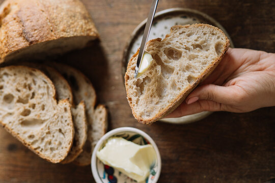 Spreading butter on crusty golden sourdough bread.
