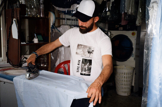 Middle Eastern Man Ironing Laundry in Local Dry Cleaning Business. 