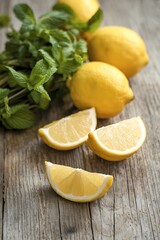 Adjacent to the leaves are three bright yellow lemons, with two of them being whole and one sliced into two wedges