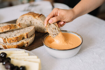 Hand dipping bread slice into creamy orange dip bowl.
