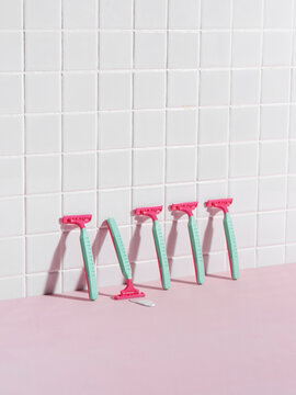 pink and green razors neatly lined up against a white tiled wall