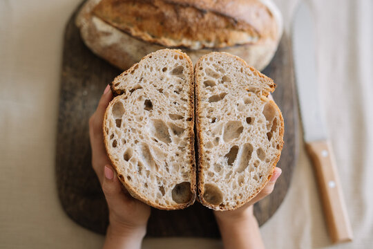 Hand holding sliced sourdough bread on cutting board.