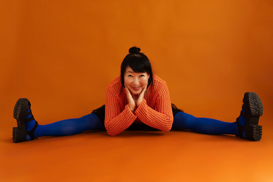 Cheerful athletic senior woman doing splits on floor