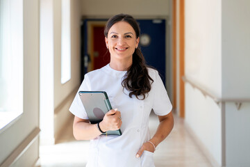 Smiling nurse holding a tablet in a hospital corridor