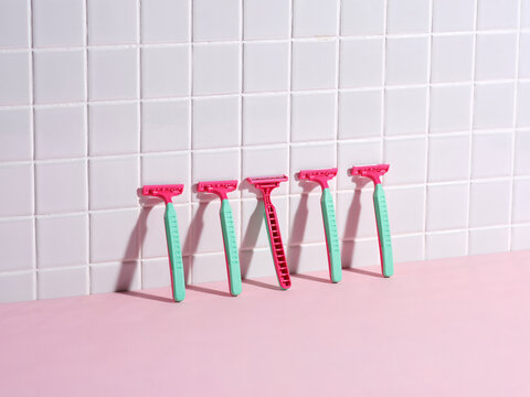 Row of Pink Razors Against White Tiled Bathroom Wall