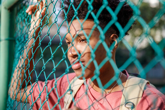 Thoughtful boy looking through chainlink fence