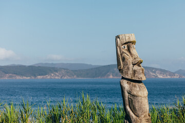 Wooden tribal sculpture overlooking serene coastline with mountains