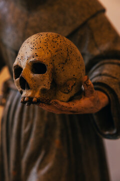 Monastic statue holding a weathered skull in dimly lit setting