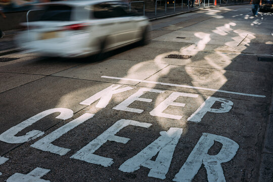Blurred car speeding over “Keep Clear” road markings in urban street
