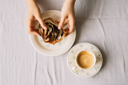 Hands breaking chocolate swirl bread slice on plate.