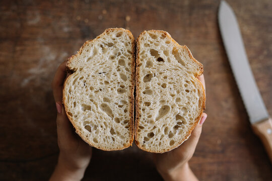 Sliced sourdough bread shown in hands on wooden table