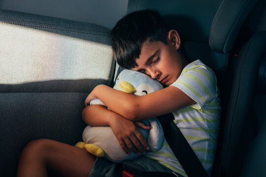 Child sleeping in car seat hugging a stuffed penguin toy