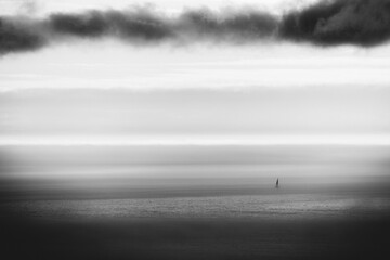 Minimalist black and white seascape with a distant lone sailboat