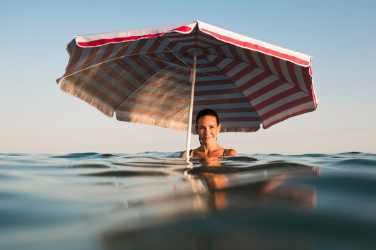 Smiling woman with beach umbrella in the sea