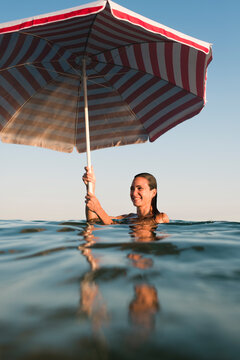 Smiling woman holding beach umbrella in the sea