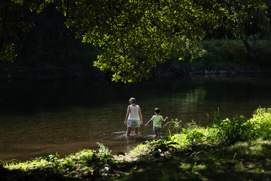 Mother and child exploring a serene riverbank under trees