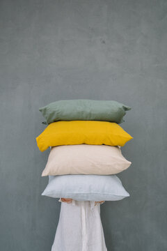 Four colorful pillows stacked against a plain grey wall