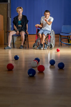 Young athlete in a wheelchair throws a ball during boccia training