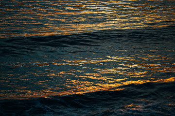 Golden sunlight reflecting over dark ocean waves during sunset