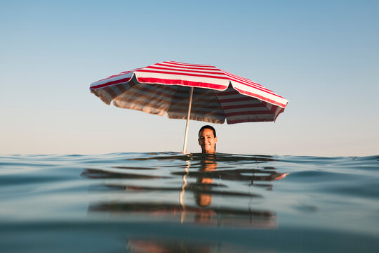 Funny summer portrait of woman in the sea with beach umbrella