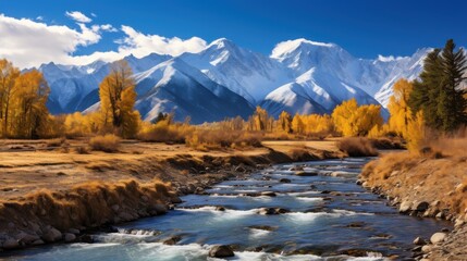 Fototapeta premium A picturesque stream winds through a vibrant autumn landscape, framed by snowy peaks under a brilliant blue sky.
