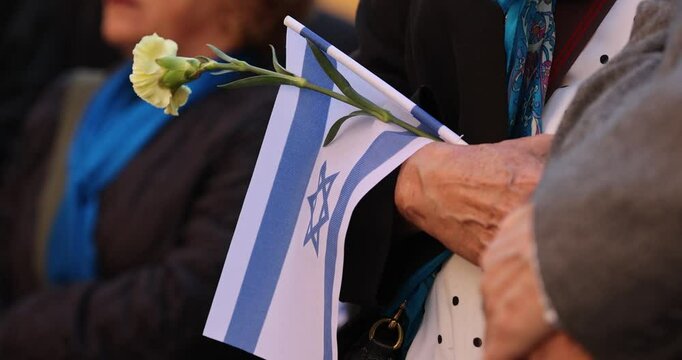 People hold the Israeli flag and flowers during a ceremony commemorating the October 2023 attacks on Israel.