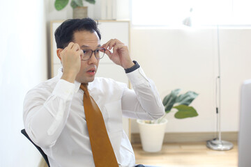 Asian Entrepreneur Thinking On Business Project While Holding Eyeglasses Sitting In Office. 