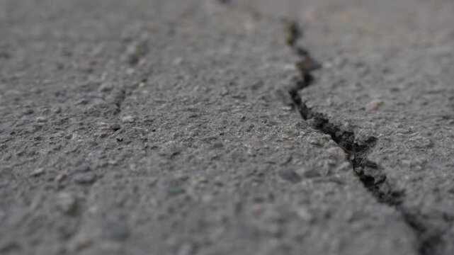 Close-up of asphalt texture with deep cracks. Part of the video is out of focus. Moving forward. Dry old cracked asphalt surface. High quality 4k footage