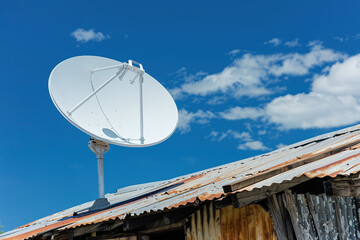 technology in poor community, contrast between dilapidated housing and new satellite dish being installed on rusty roof