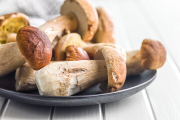 Fresh boletus mushrooms on plate on white table.