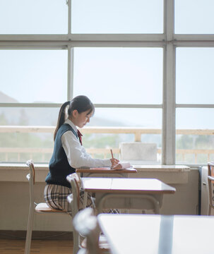 学校の窓際の席で勉強をしている女子中学生