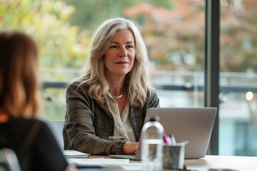 Blonde businesswoman in casual attire using laptop during collaborative team meeting in modern office setting