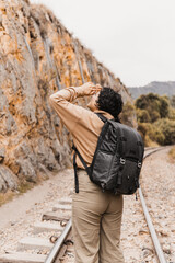 A traveler stops to look up at towering canyon walls while standing on a railroad track, surrounded by nature