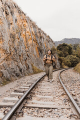 A young woman hikes along a railroad track surrounded by towering rock cliffs and lush greenery