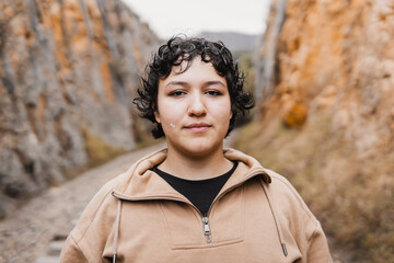 A close-up portrait of a woman standing in a canyon, surrounded by rocky cliffs, looking into the camera