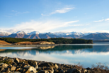 A breathtaking view of Lake Pukaki with snow-capped mountains reflecting on the still water during a clear day with vibrant colors and expansive scenery in the South Island of New Zealand