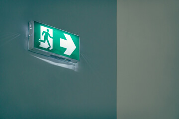 green emergency exit or fire exit hanging sign showing the way to escape from building of hospital or hotel at night time