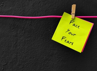 Yellow note on black copy space background written FACE YOUR FEARS , motivate oneself to confront...