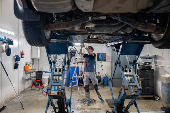 car mechanic standing under lifted car and fixing car in garage