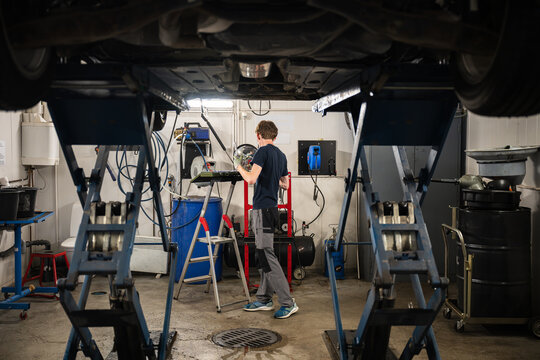 car mechanic standing under lifted car and fixing car in garage