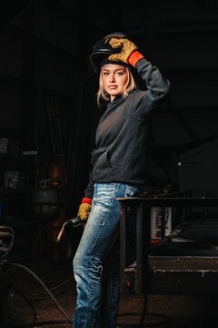 Woman in work gloves and welding helmet, holding a torch in a workshop