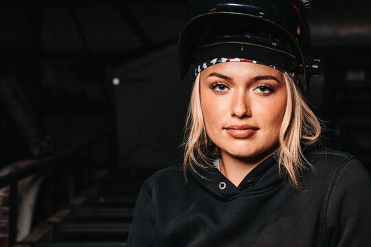 Woman in work gloves and welding helmet, holding a torch in a workshop