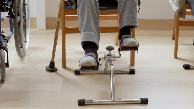 Elderly man engaging in leg exercises with a pedal exerciser during rehabilitation at a nursing home