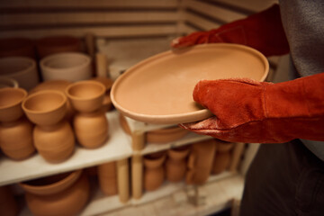 Ceramist removing a clay plate from a kiln in his workshop