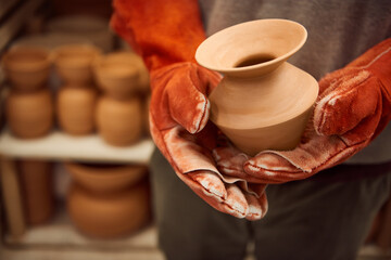 Ceramist standing with a clay vase by a kiln in his workshop