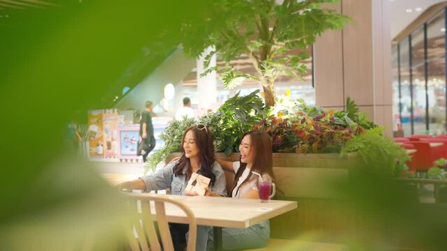 Happy Asian daughter give gift box to mature mother celebration birthday party or mother's day during shopping at shopping mall. Mom and adult child girl using smartphone taking selfie together.