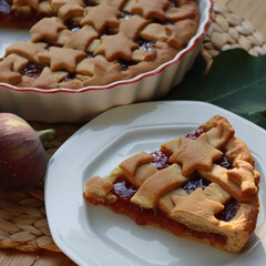 Slice of tart with dark fig jam on a white dessert plate  on wooden table with fresh figs and autumnal leaves